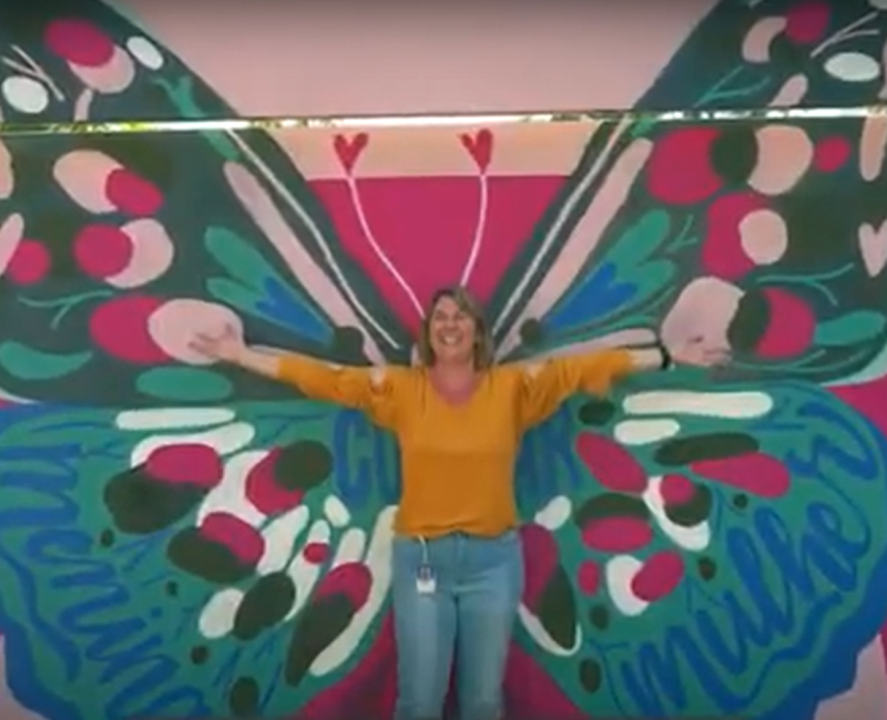 woman in front of butterfly wing mural- arms outstretched for international women's day