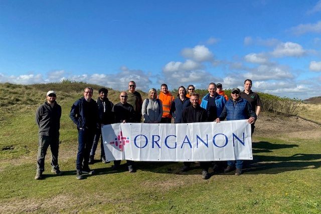 Organon employee volunteer event. Group of employees in field holding sign.